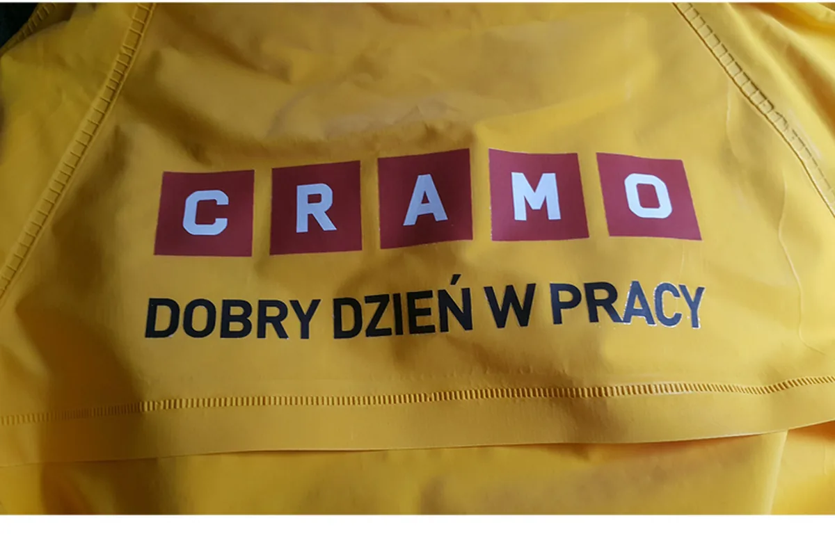 Nadruk logo CRAMO z hasłem na żółtej kurtce roboczej, zbliżenie