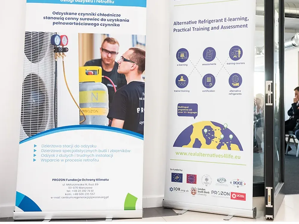 Dwa rollupy reklamowe z grafiką firmową ustawione przy wejściu na salę konferencyjną